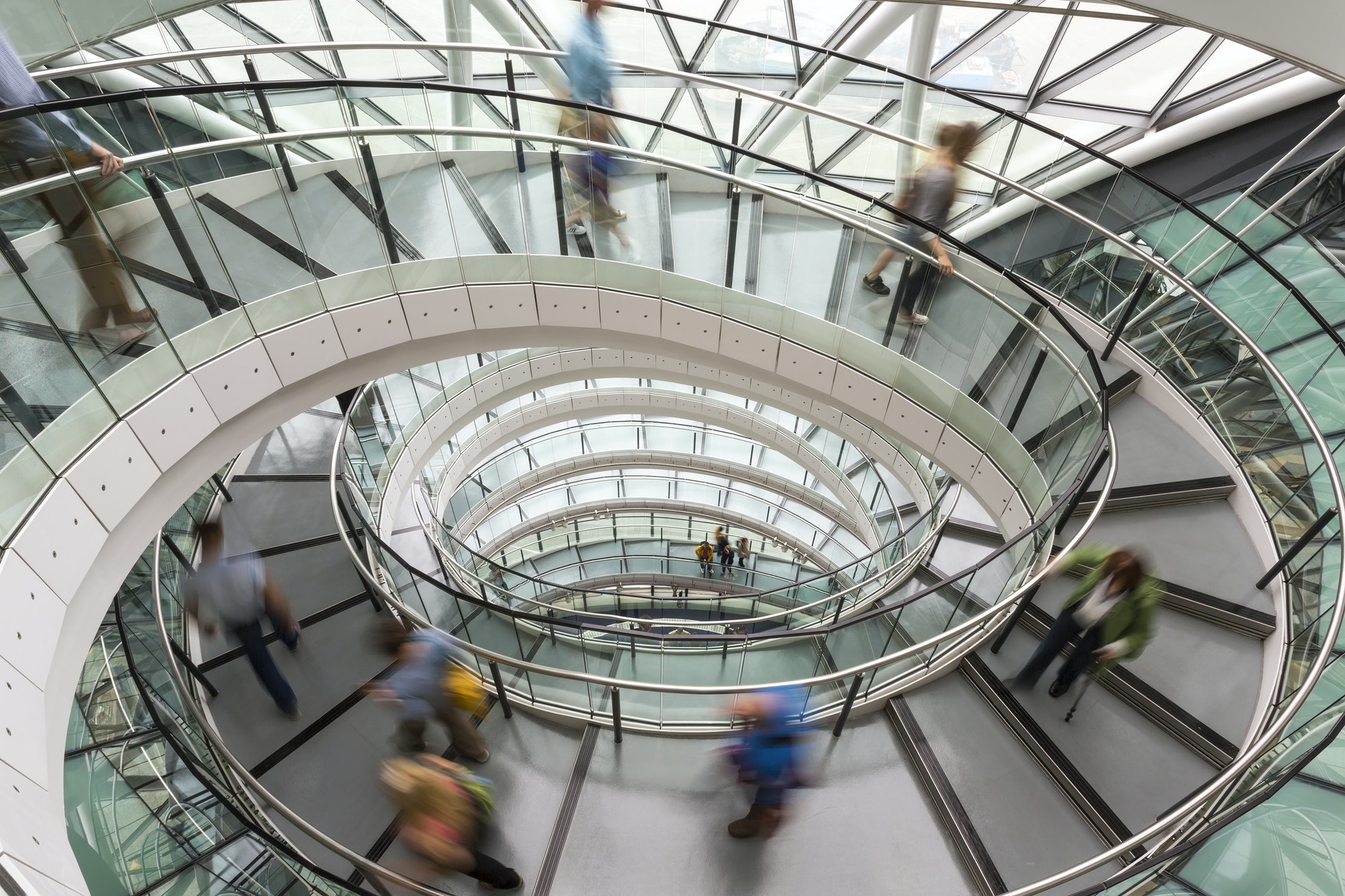 Interior view of building with people walking along glass and metal spiral staircase.